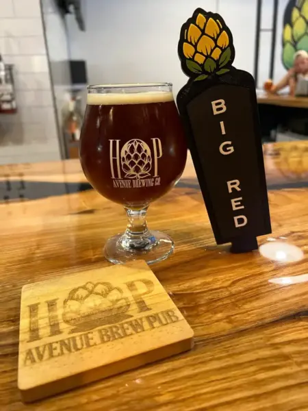 Big Red Irish Red Ale in a branded glass next to its tap handle at Hop Avenue Brew Pub in Bridge City.