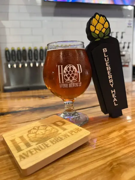 "Blueberry Heal fruited wheat beer in a branded glass next to its tap handle at Hop Avenue Brew Pub in Bridge City."