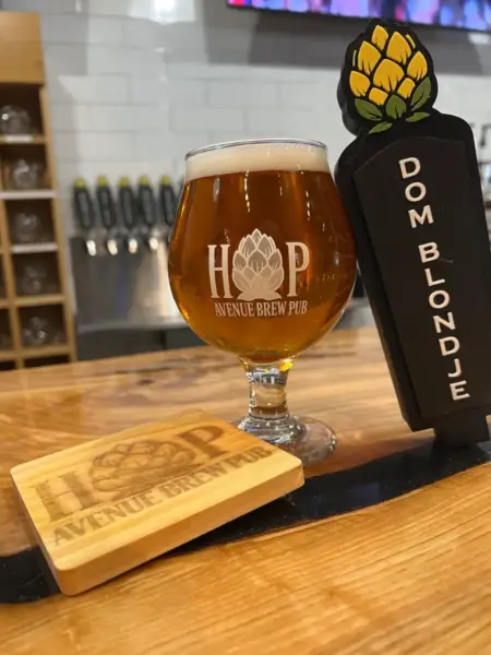"Dom Blondje Belgian Blonde Ale in a branded glass next to its tap handle at Hop Avenue Brew Pub in Bridge City."