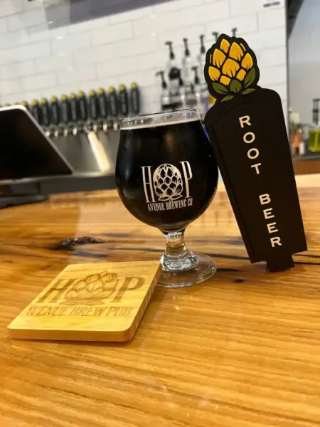 "Hop Hard Root Beer in a branded glass next to a tap handle at Hop Avenue Brew Pub in Bridge City."