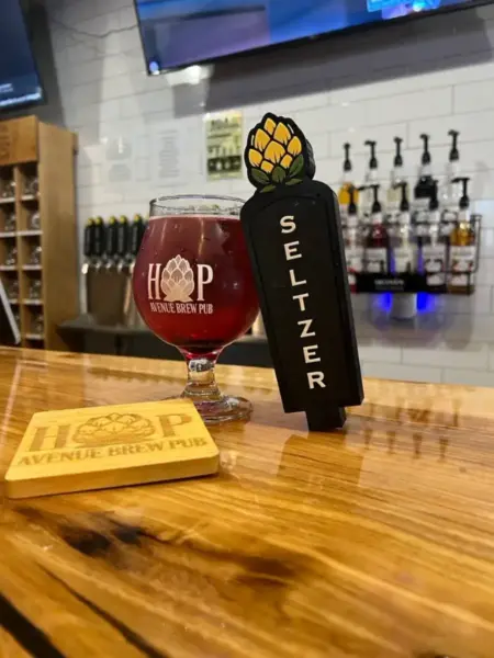 "Vibrant craft hard seltzer in a branded glass next to a Seltzer tap handle at Hop Avenue Brew Pub in Bridge City."