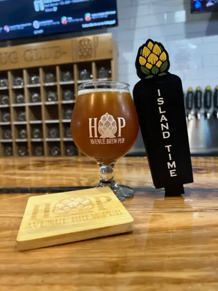 "A glass of Island Time craft beer next to a branded coaster and Mug Club rack at Hop Avenue Brew Pub in Bridge City