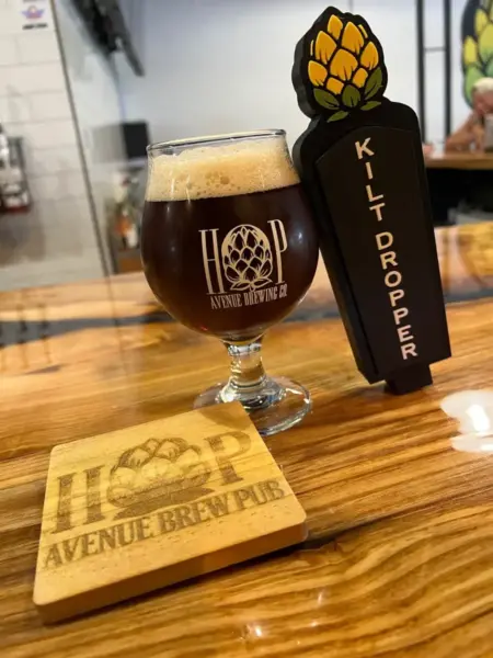 Kilt Dropper Scotch Scottish Ale in a branded snifter glass next to its tap handle at Hop Avenue Brew Pub in Bridge City.