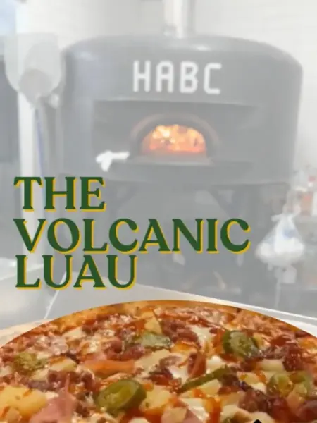 "The Volcanic Luau pizza with spicy jalapeños, sweet pineapple, and ham in Bridge City, in front of a brick oven."