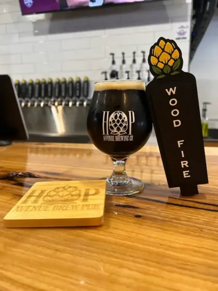 "Wood Fired Smoked Porter in a branded glass next to its custom tap handle at Hop Avenue Brew Pub in Bridge City."