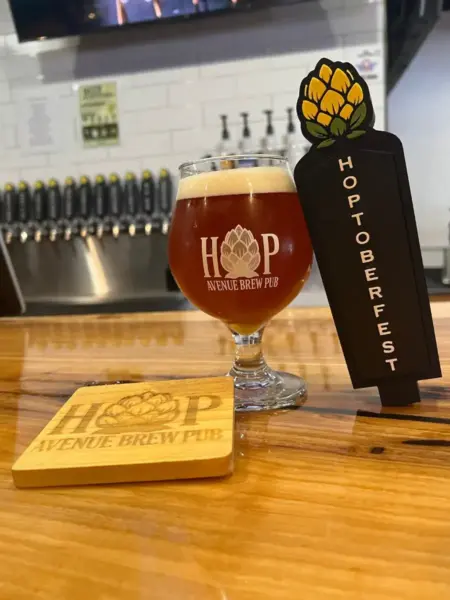 "Hoptoberfest German Style Lager in a branded glass next to its tap handle at Hop Avenue Brew Pub in Bridge City."