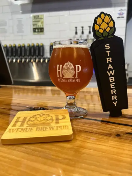 "Strawberry Fields Fruited Wheat Beer next to its custom tap handle at Hop Avenue Brew Pub in Bridge City."